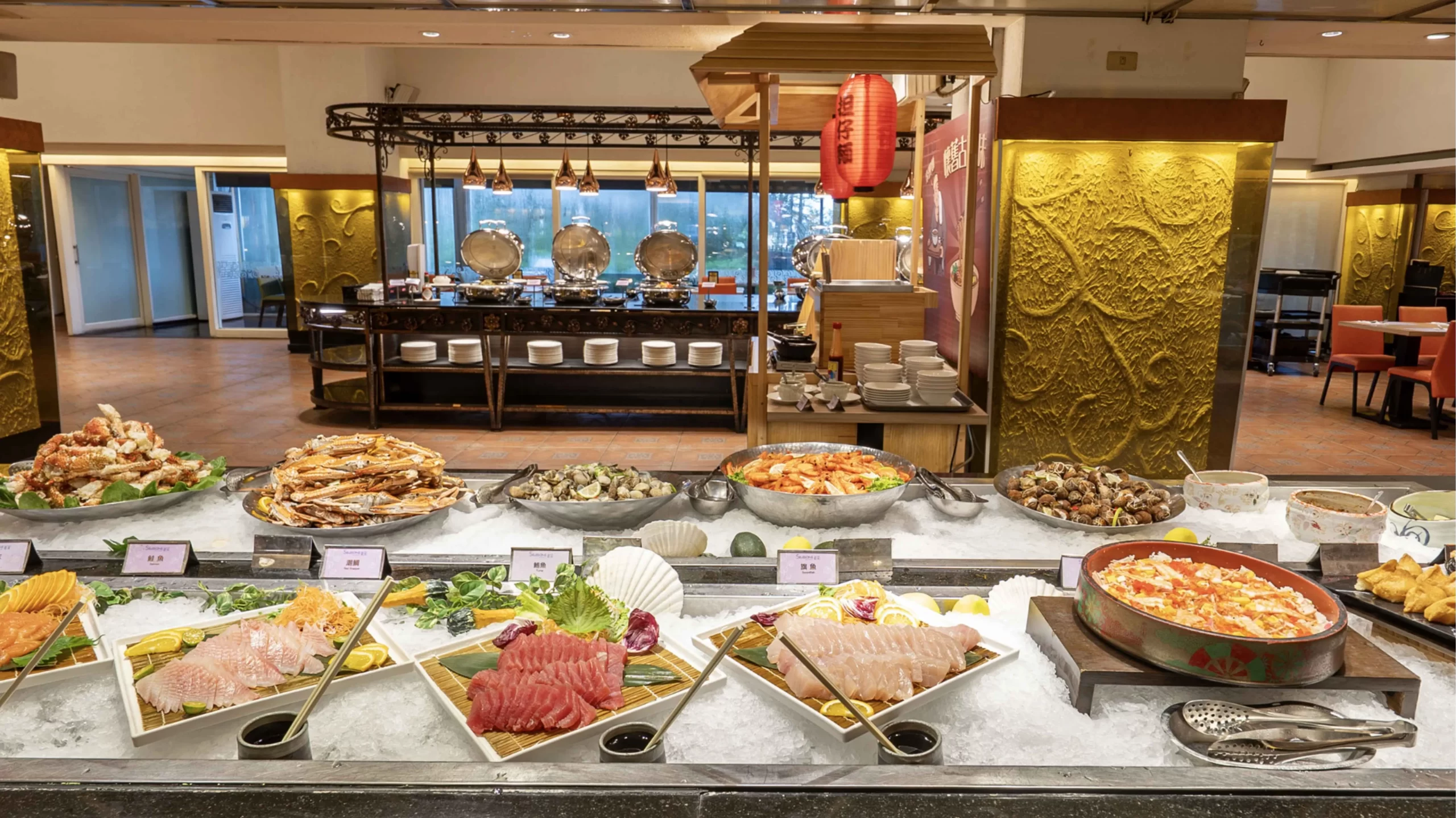 台中清新溫泉飯店新采自助百匯的海鮮餐檯,鋪滿冰鎮的生魚片、螃蟹、熟蝦與風螺,後方設有日式擔仔麵攤與熱食區。